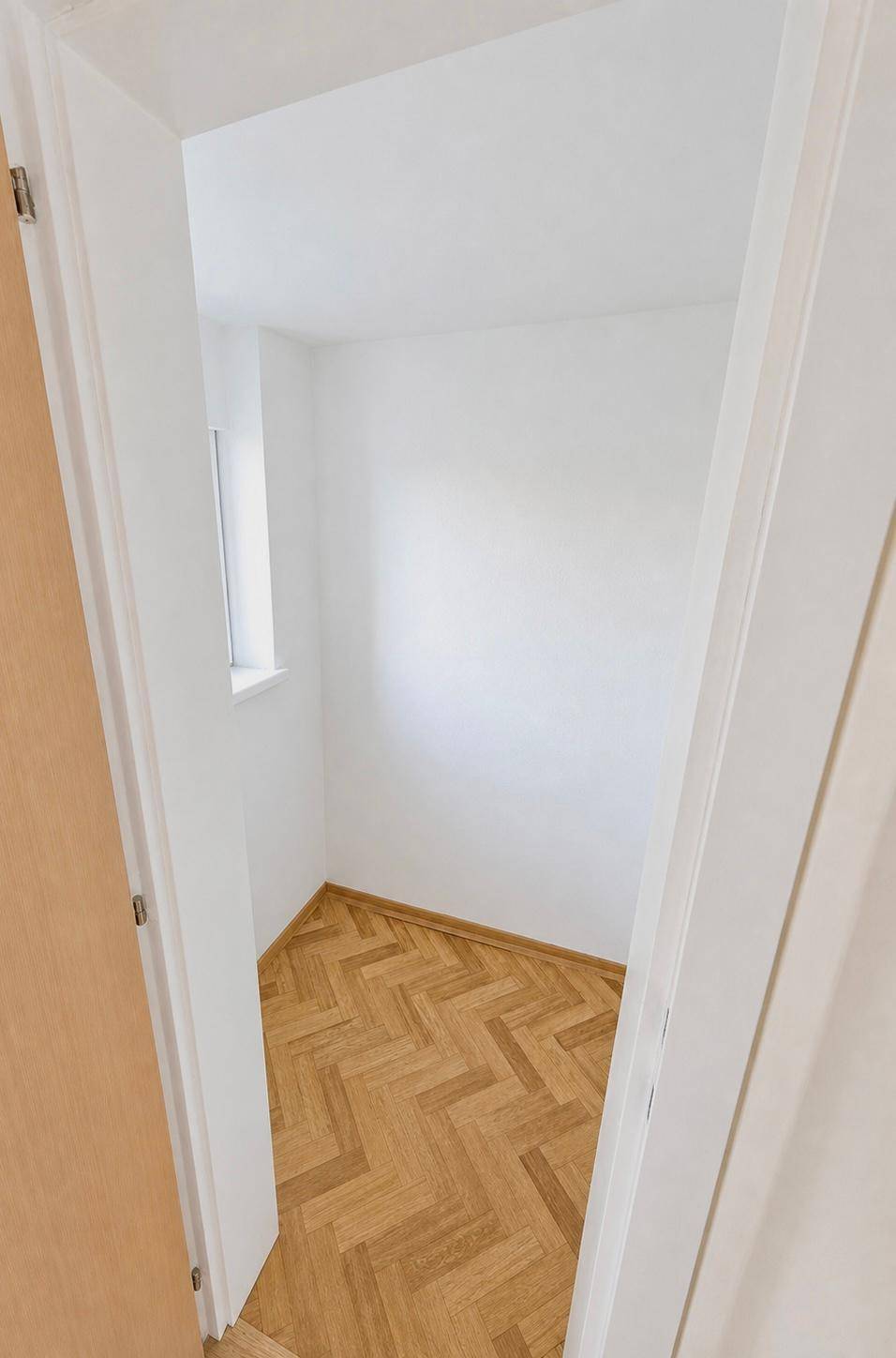 Kleiner, heller Raum mit Fischgrätparkettboden und einem Fenster, ideal als Büro.