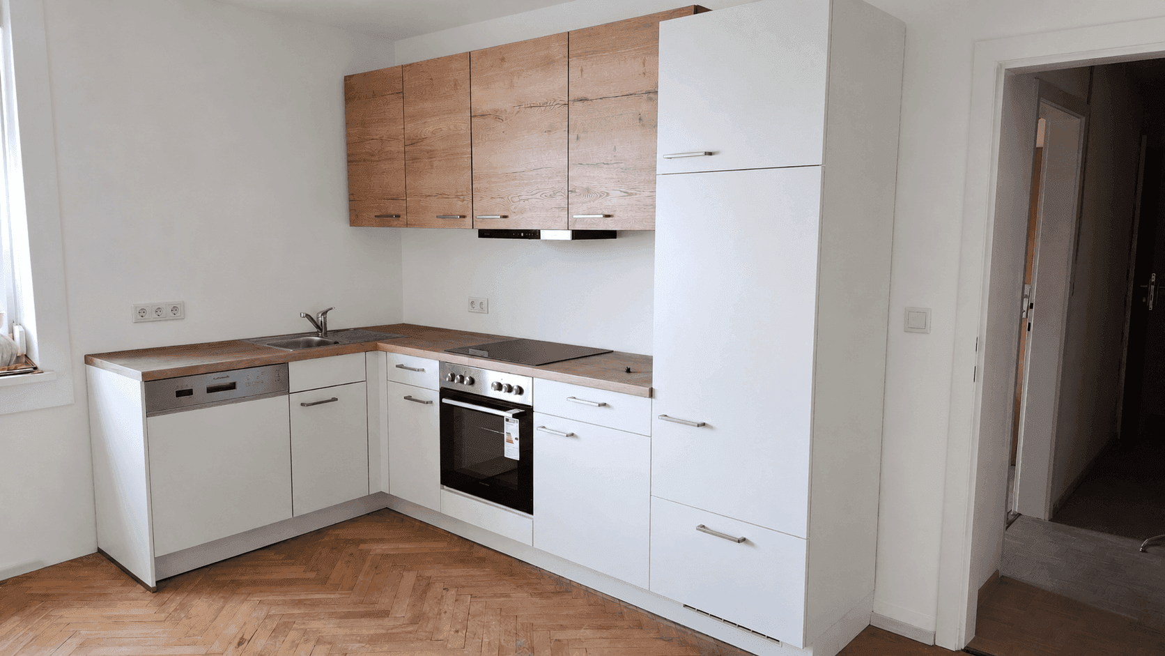 Moderne Einbauküche mit weißen und holzfarbenen Schränken, ausgestattet mit Geräten.