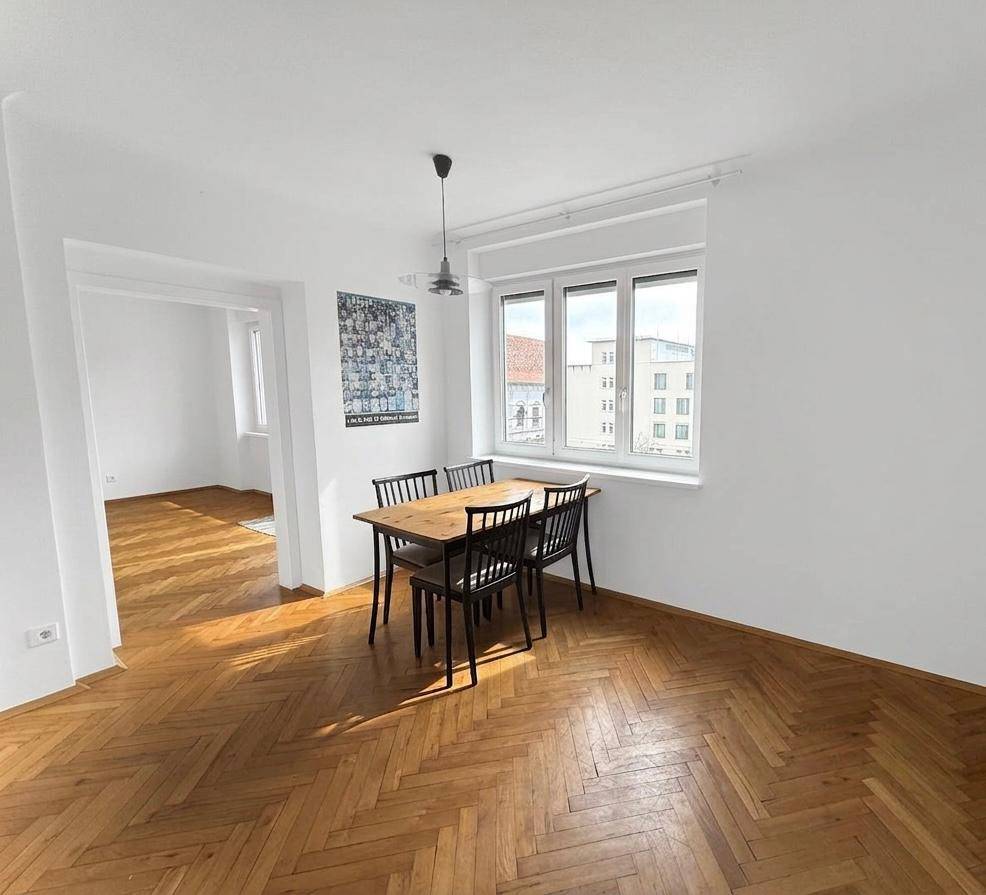 Heller Essbereich mit Holztisch und Stühlen, verbunden mit einem weiteren Raum.