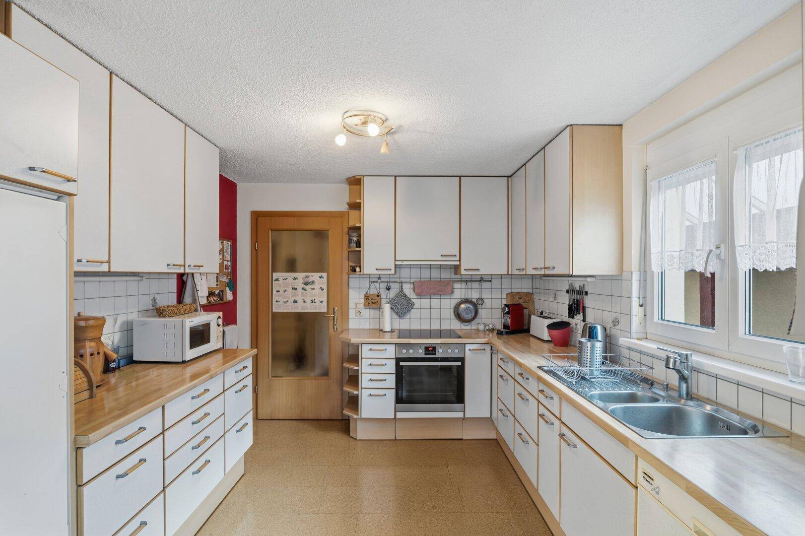 Geräumige Küche mit weißen Einbauschränken, Holztheken und integrierten Küchengeräten.