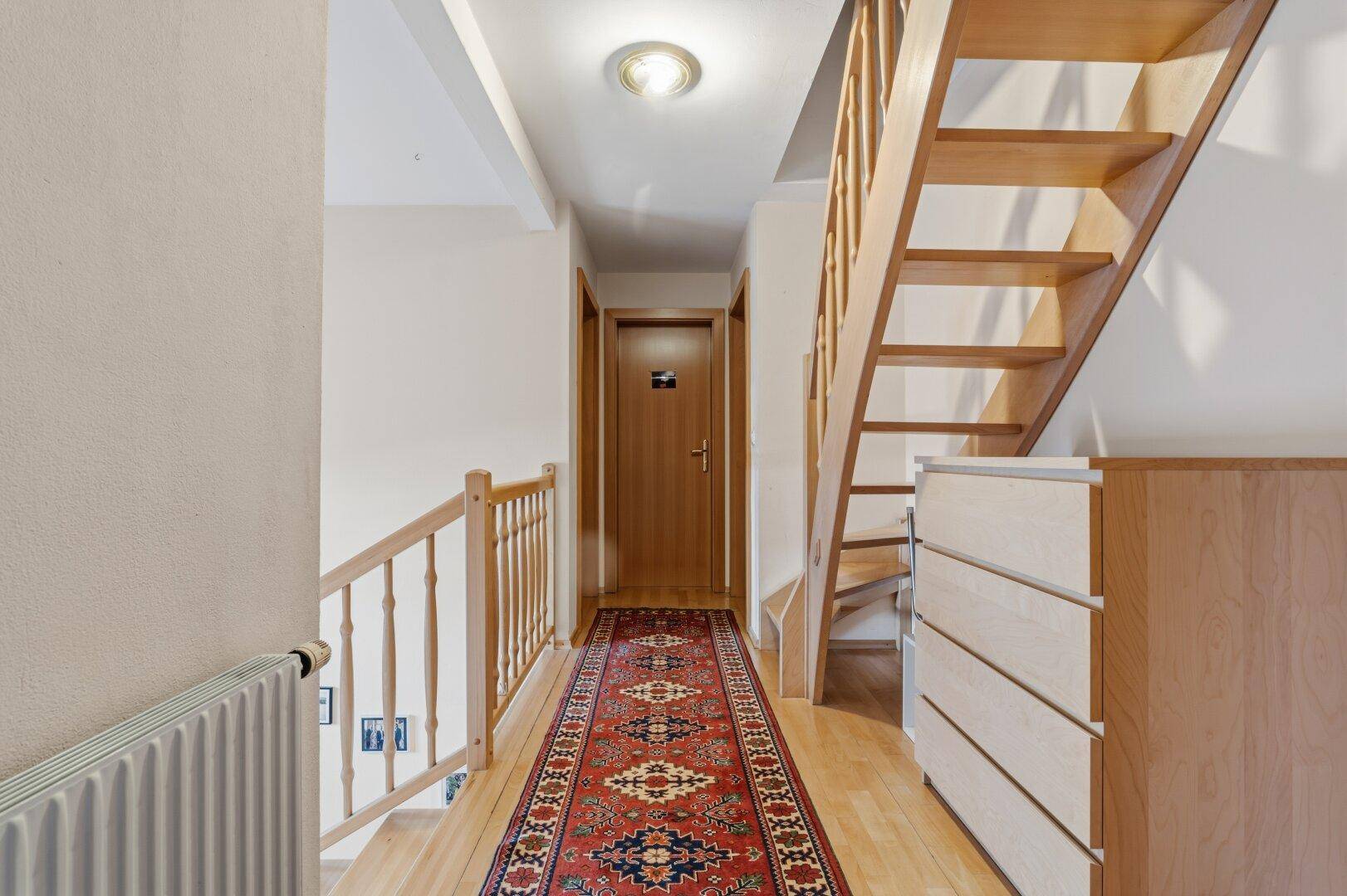 Heller Flur mit Holztreppe, Teppichläufer und Zugang zu weiteren Räumen.