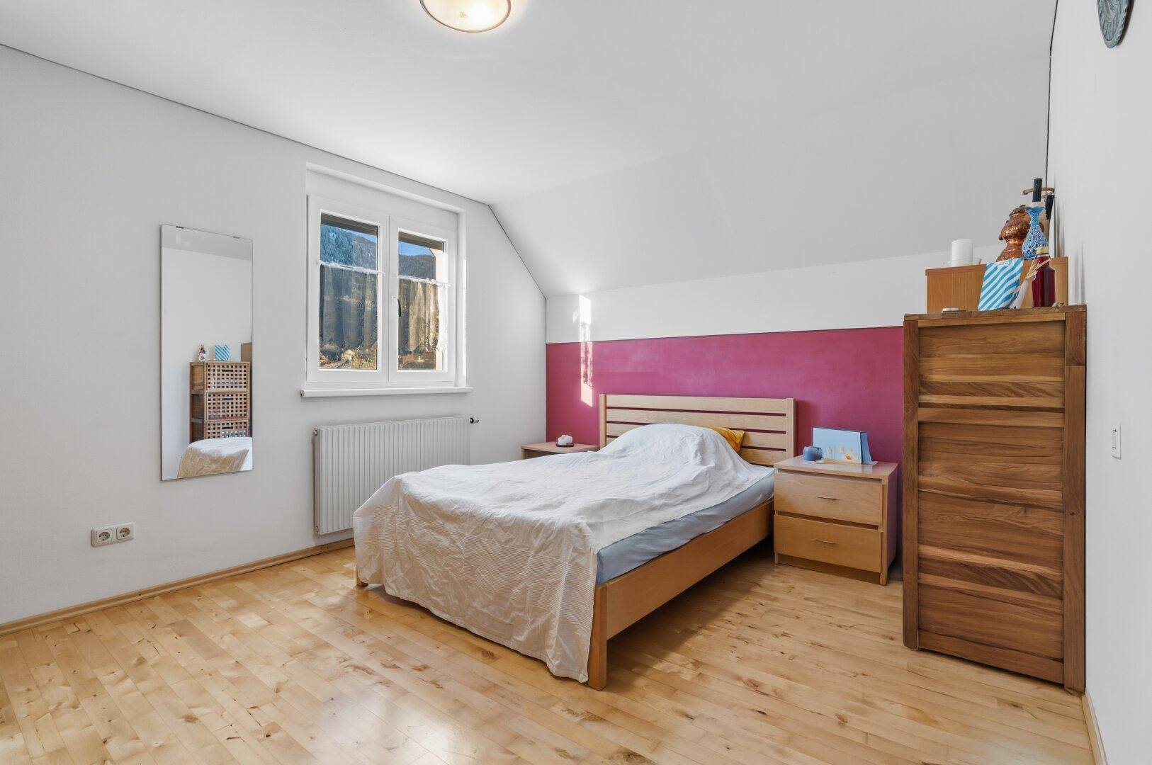 Schlafzimmer im Dachgeschoss mit Holzboden, Dachschräge und farbiger Akzentwand.