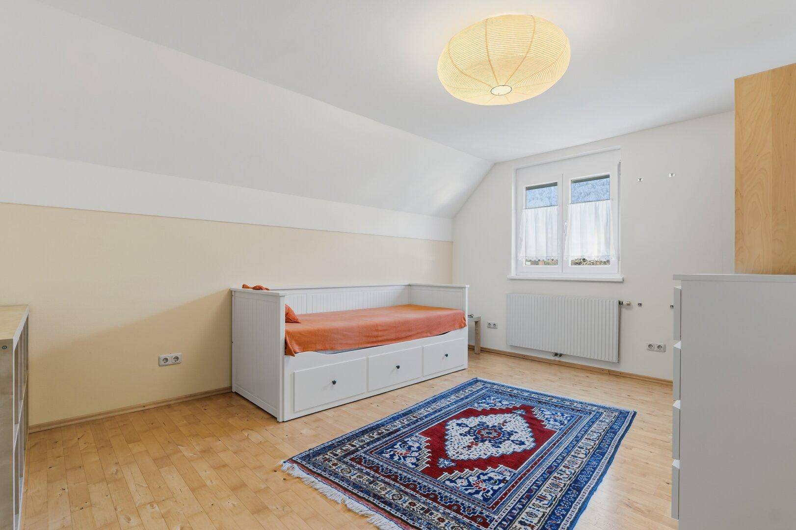 Helles Schlafzimmer mit Tagesbett, Holzboden und Dachschräge, ideal als Gästezimmer.