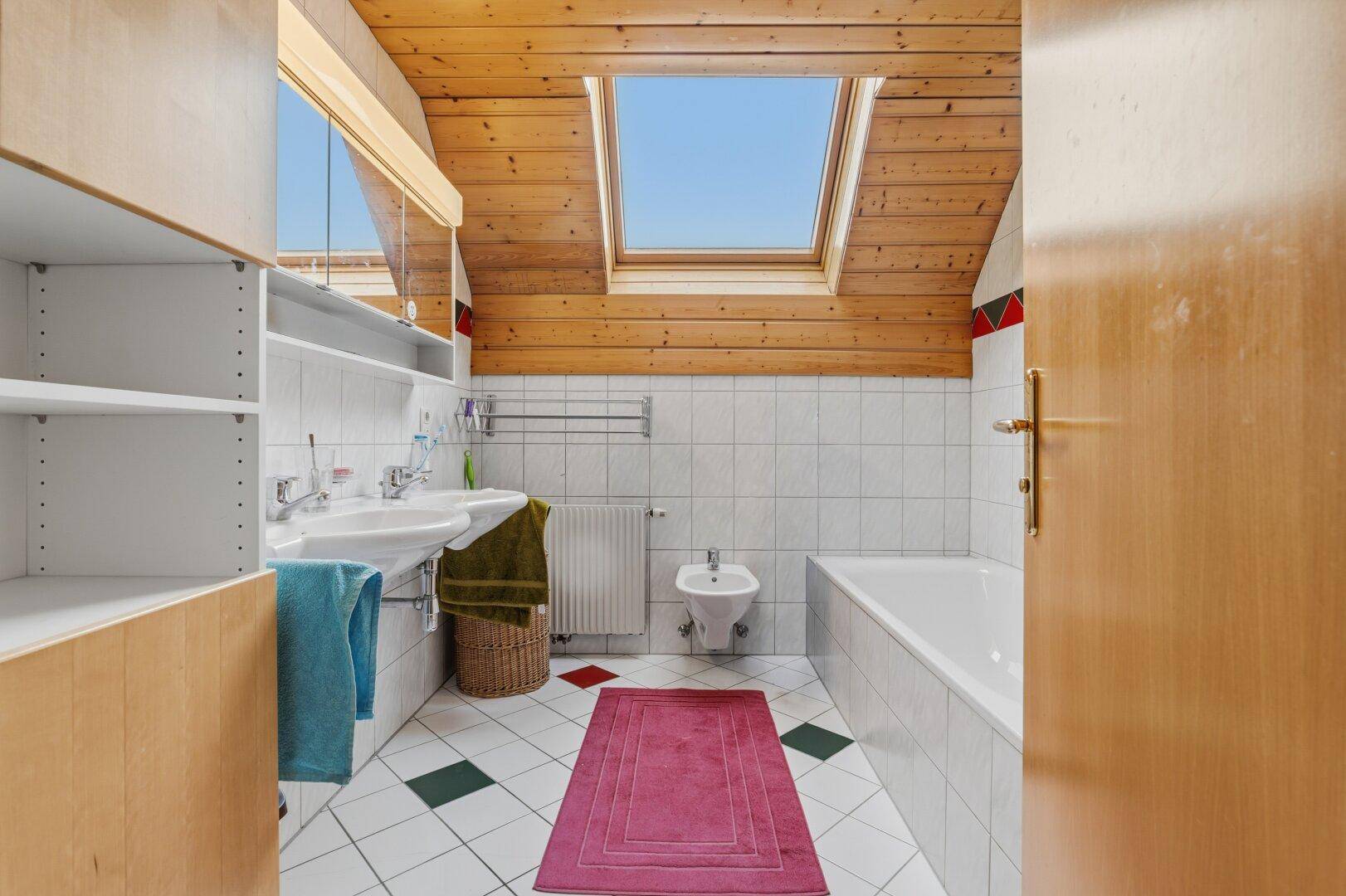 Badezimmer im Dachgeschoss mit Holzdecke, Dachfenster, Doppelwaschbecken und Bidet.