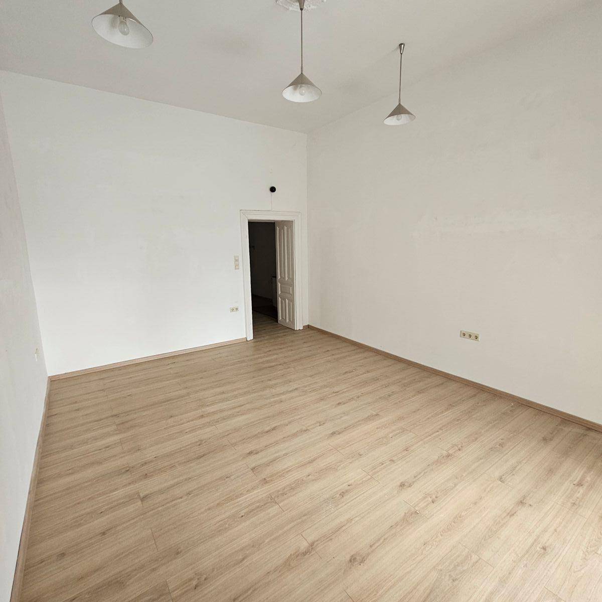 Heller, leerer Raum mit Laminatboden und weißen Wänden, bereit zur individuellen Gestaltung.
