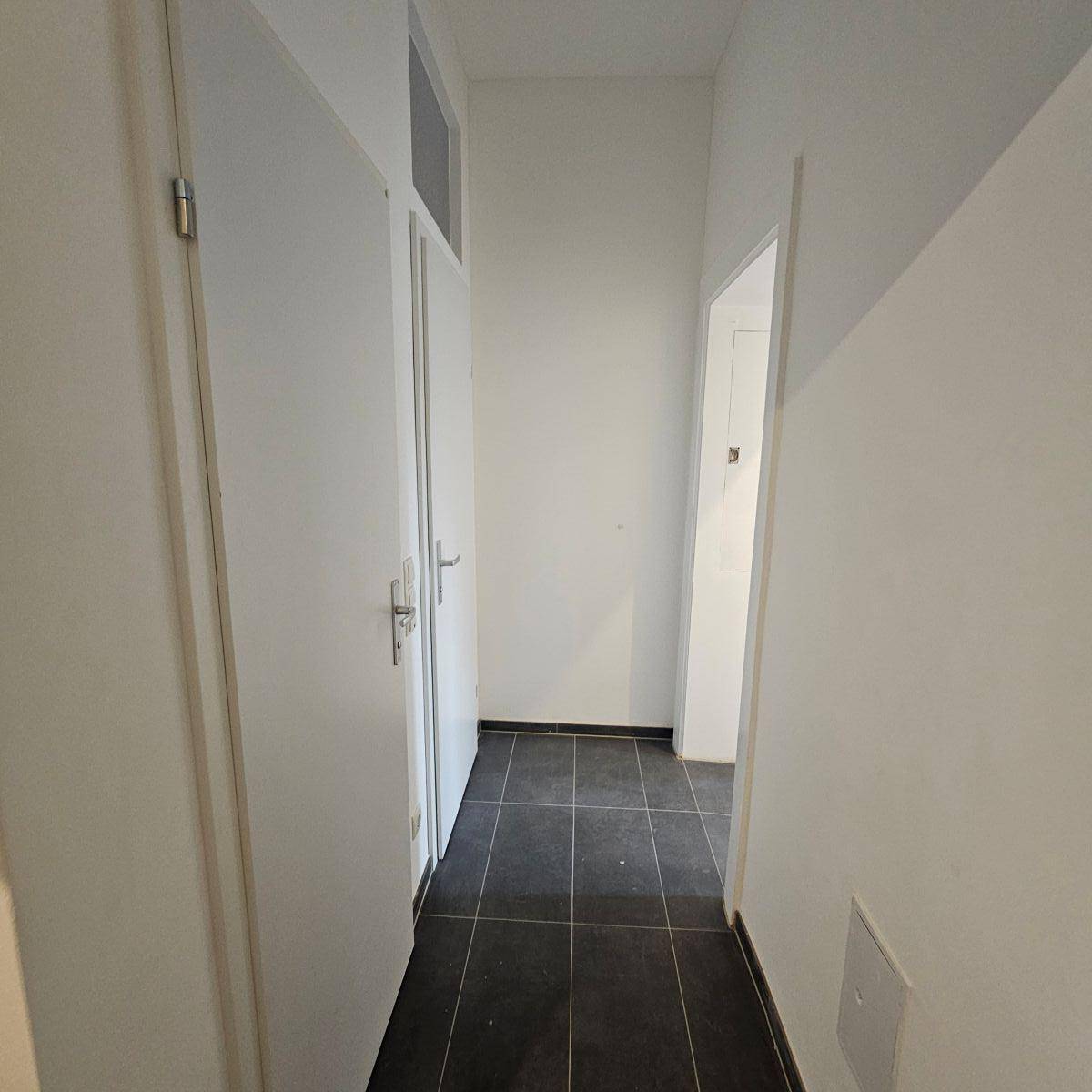 Heller Flur mit dunklem Fliesenboden und weißen Türen, der zu weiteren Räumen führt.