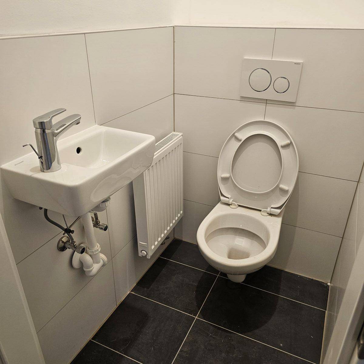 Kleines Gäste-WC mit wandhängender Toilette, kleinem Waschbecken und dunklem Fliesenboden.