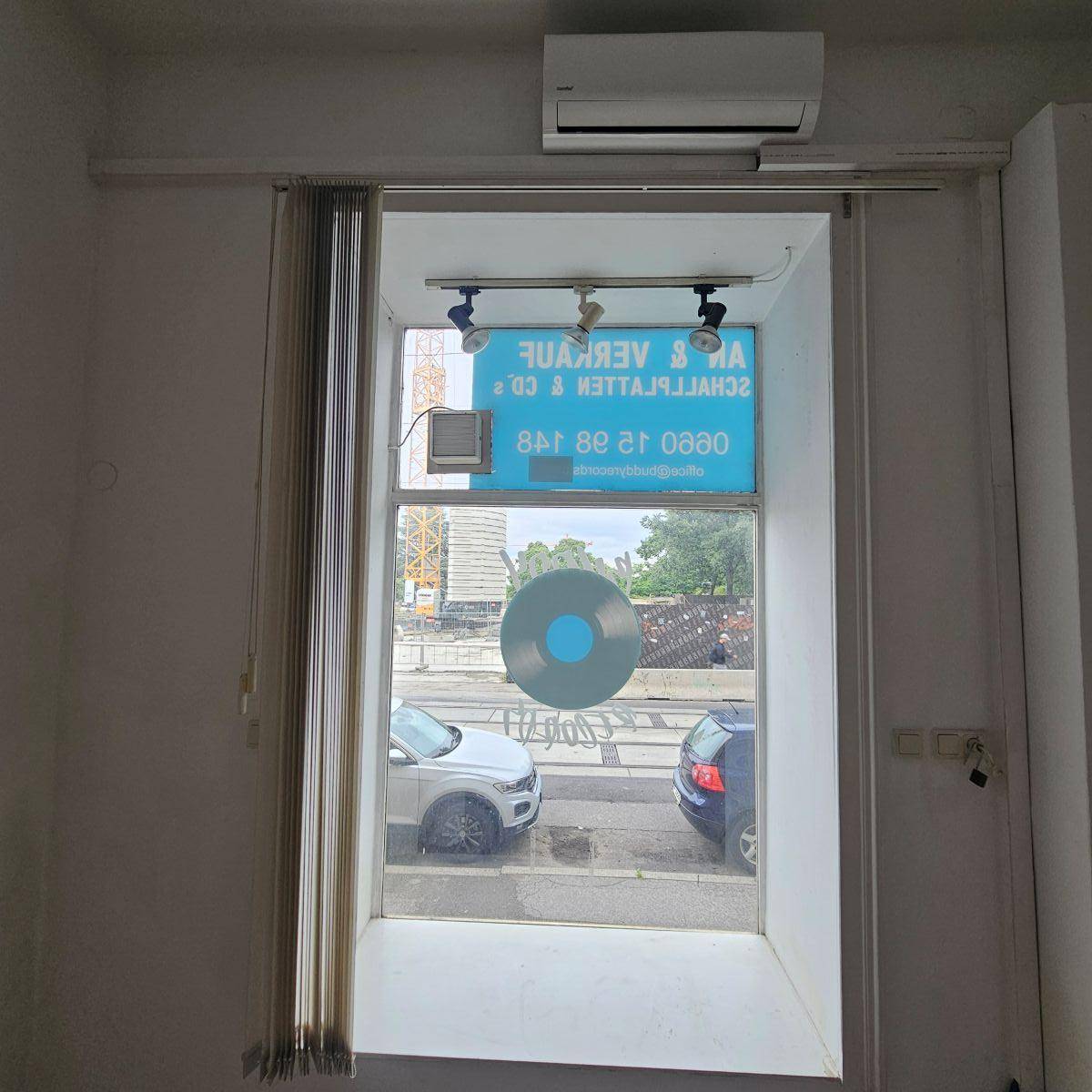 Blick aus einem Fenster auf die Straße mit parkenden Autos und einem Baukran im Hintergrund.