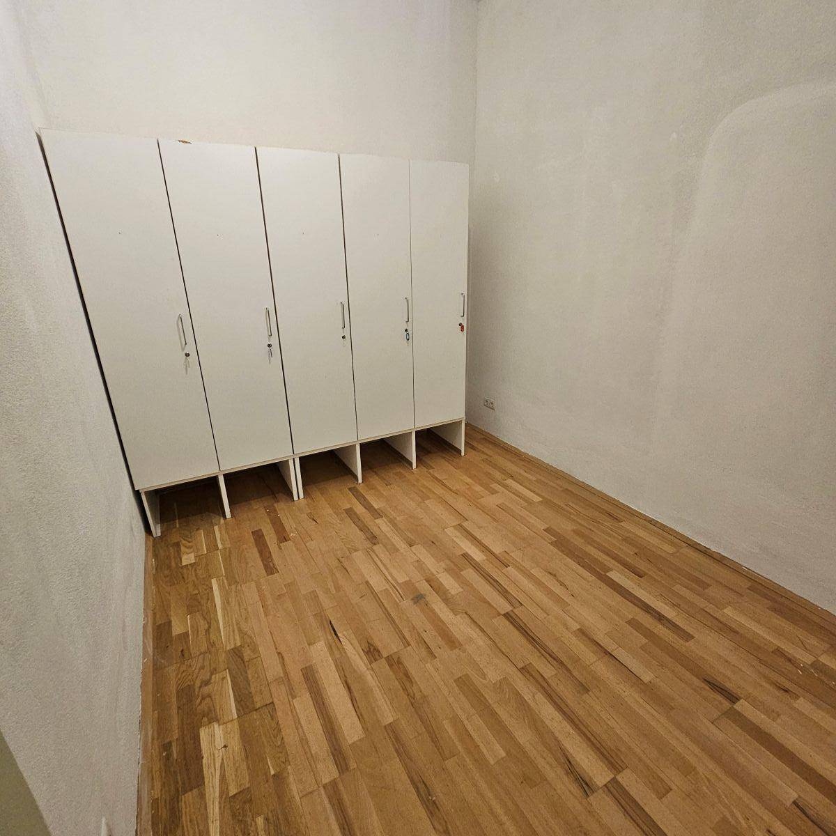 Raum mit Holzparkettboden und einer Reihe weißer Schränke entlang einer Wand, ideal als Lagerraum.