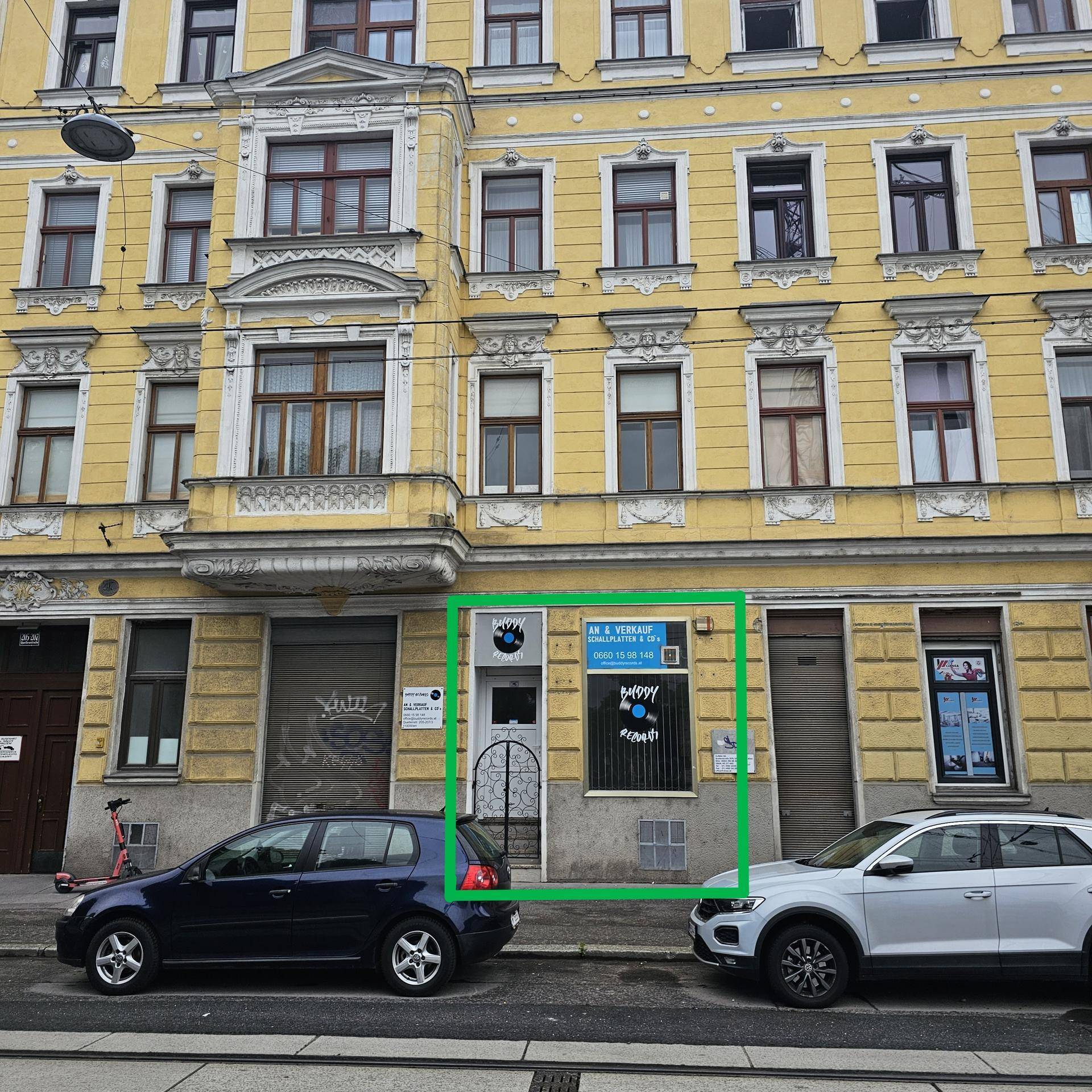 Gesamtansicht der gelben Fassade eines Altbaus mit einem Ladenlokal im Erdgeschoss und parkenden Autos.