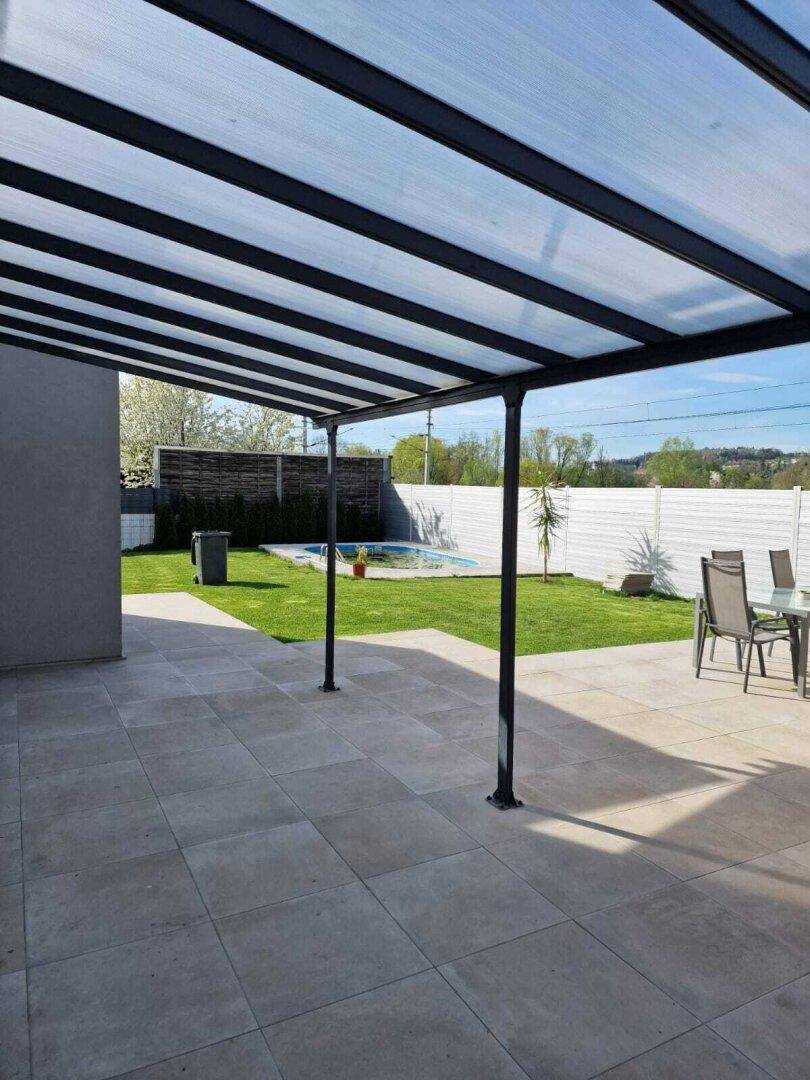 Überdachte Terrasse mit Fliesenboden und Gartenmöbeln, Blick auf den Pool und die grüne Umgebung.