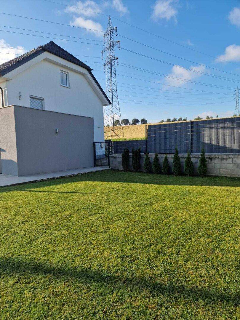 Gepflegter Rasenbereich neben dem Haus mit Hecke und Blick auf die umliegende Landschaft.