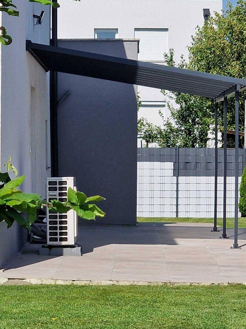 Überdachte Terrasse mit Fliesenboden und einer Wärmepumpe an der Hauswand.