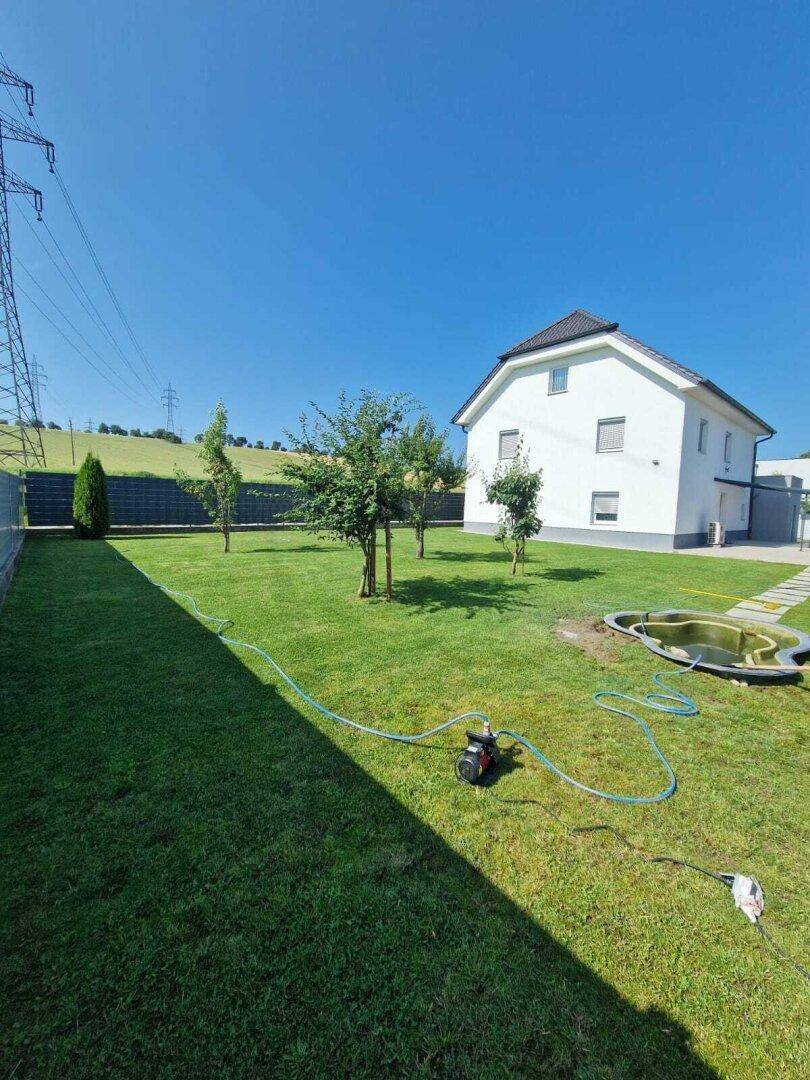 Weitläufiger Garten mit Rasenfläche, Bäumen und einem kleinen Teich vor dem Haus.