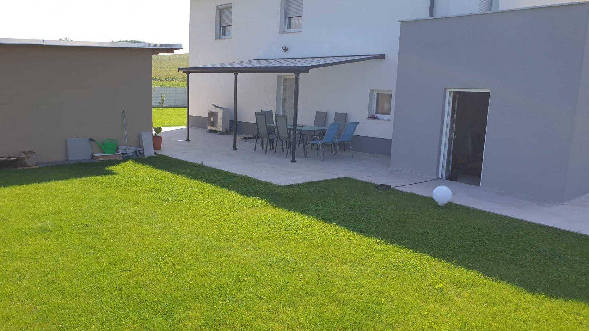 Große Terrasse mit Gartenmöbeln und Rasenfläche neben dem modernen Einfamilienhaus.