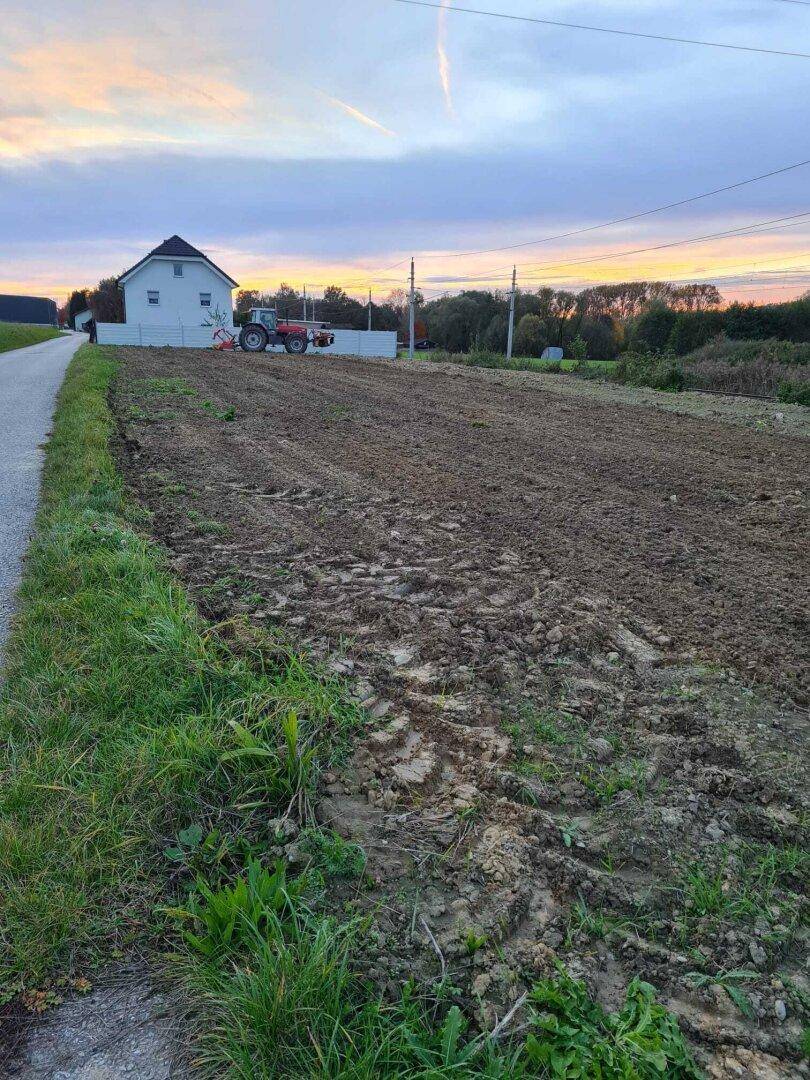 Weitläufiges Feld mit Ackerboden und einem Haus in der Ferne bei Sonnenuntergang.