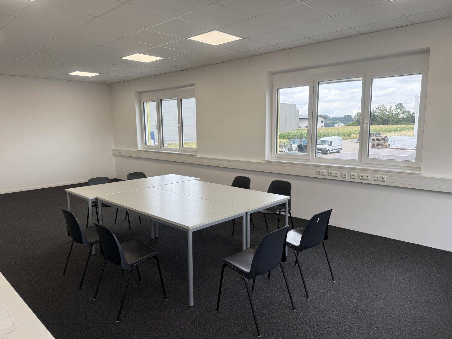 Funktionaler Besprechungsraum mit Teppichboden und Fenstern, die viel Tageslicht hereinlassen.