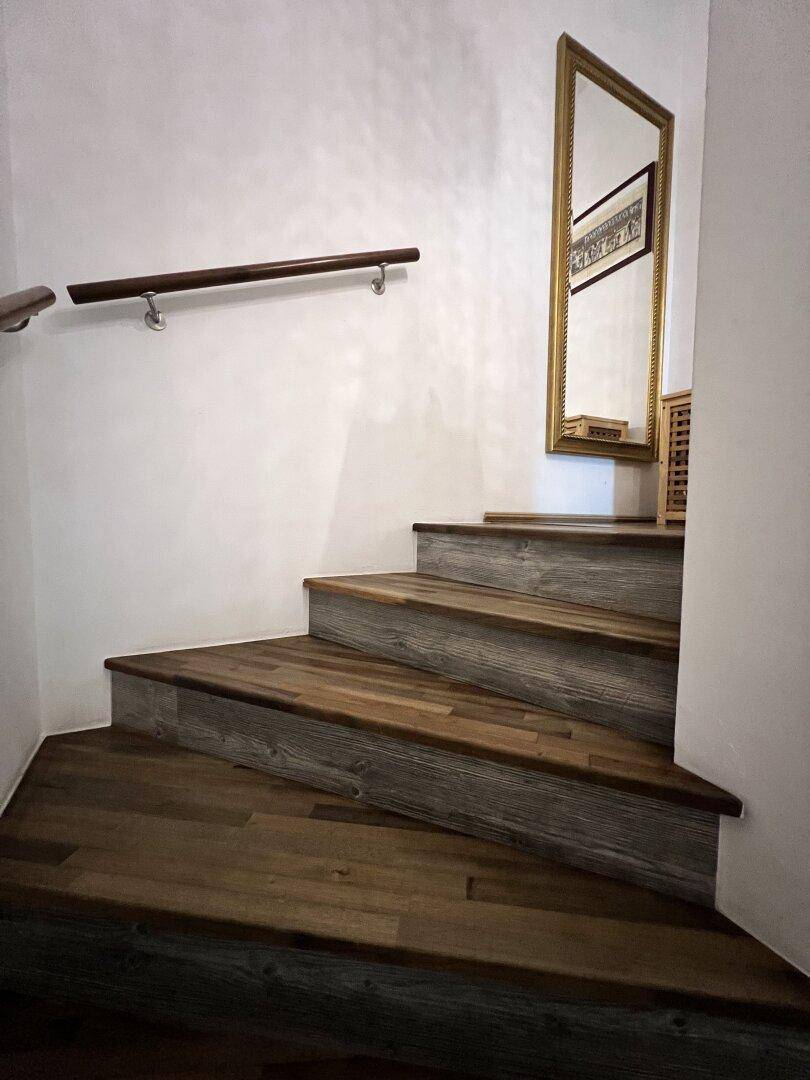Holztreppe mit Handlauf und Spiegel, die die verschiedenen Etagen verbindet.