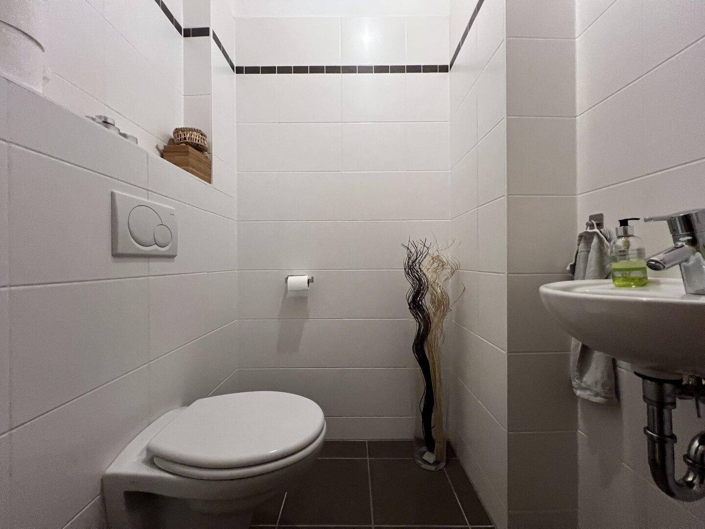Modern gefliestes Gäste-WC mit Wand-WC und kleinem Waschbecken.