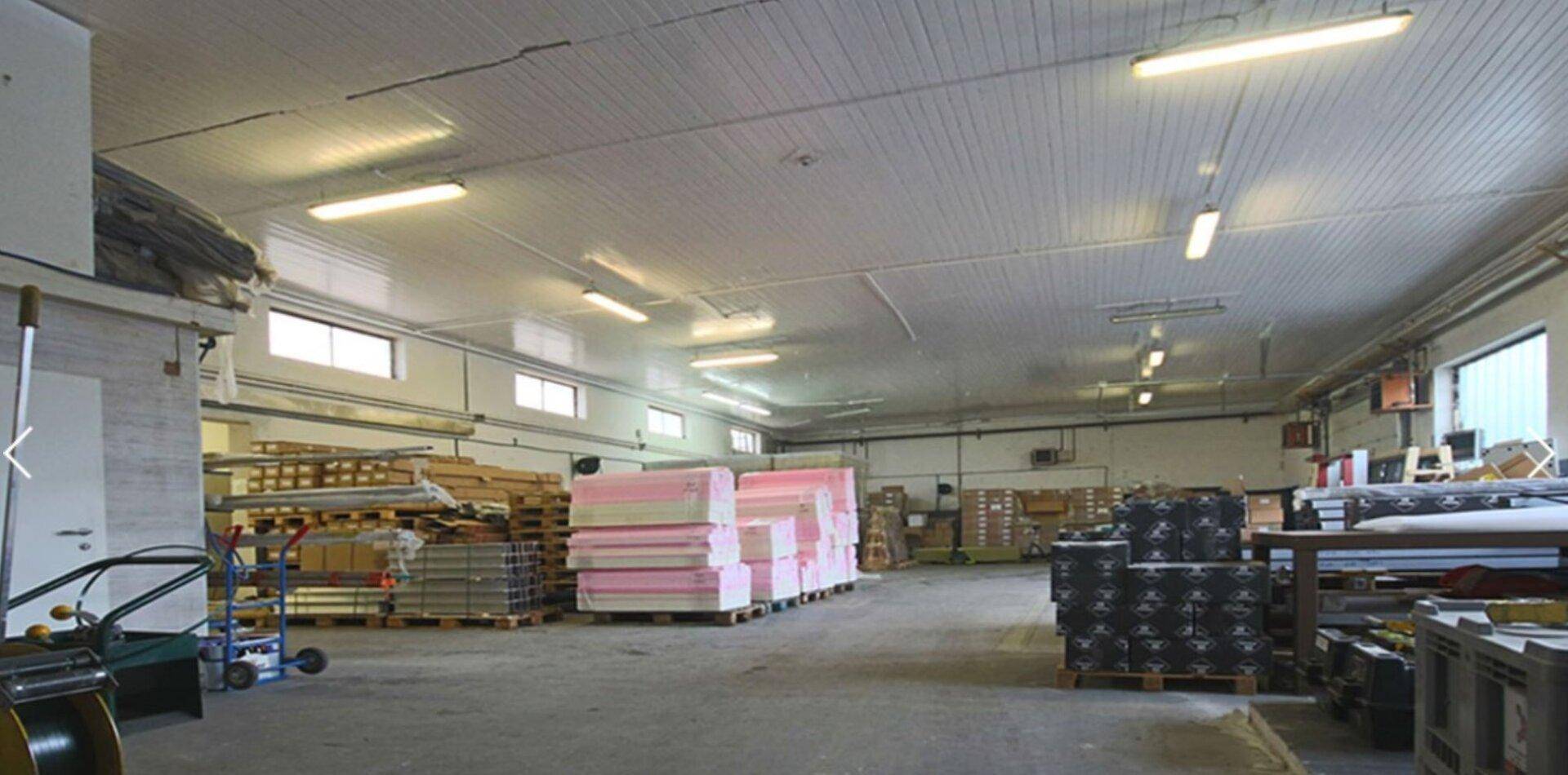 Geräumige Lagerhalle mit hohen Decken, Leuchtstoffröhren und gestapelten Waren auf Paletten.
