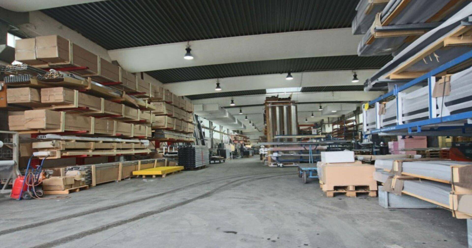 Industrielle Lagerhalle mit hohen Regalen, gefüllt mit Materialien und einem dunklen Wellblechdach.