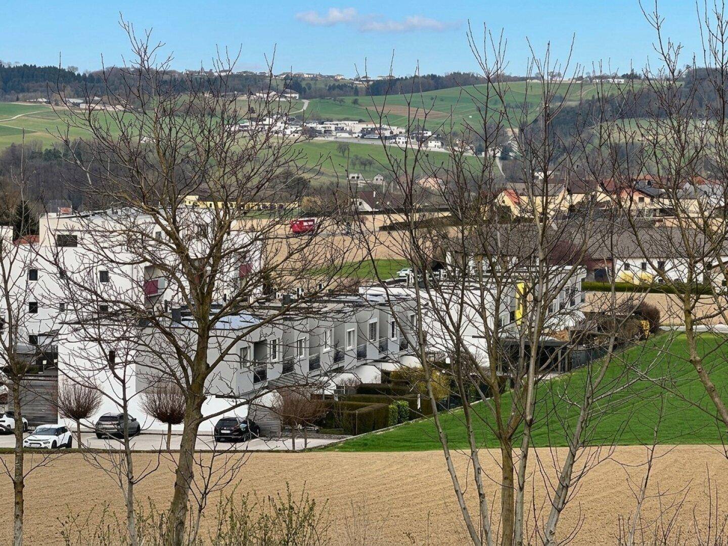 Weitläufiger Blick über eine Wohnsiedlung mit grünen Hügeln im Hintergrund.