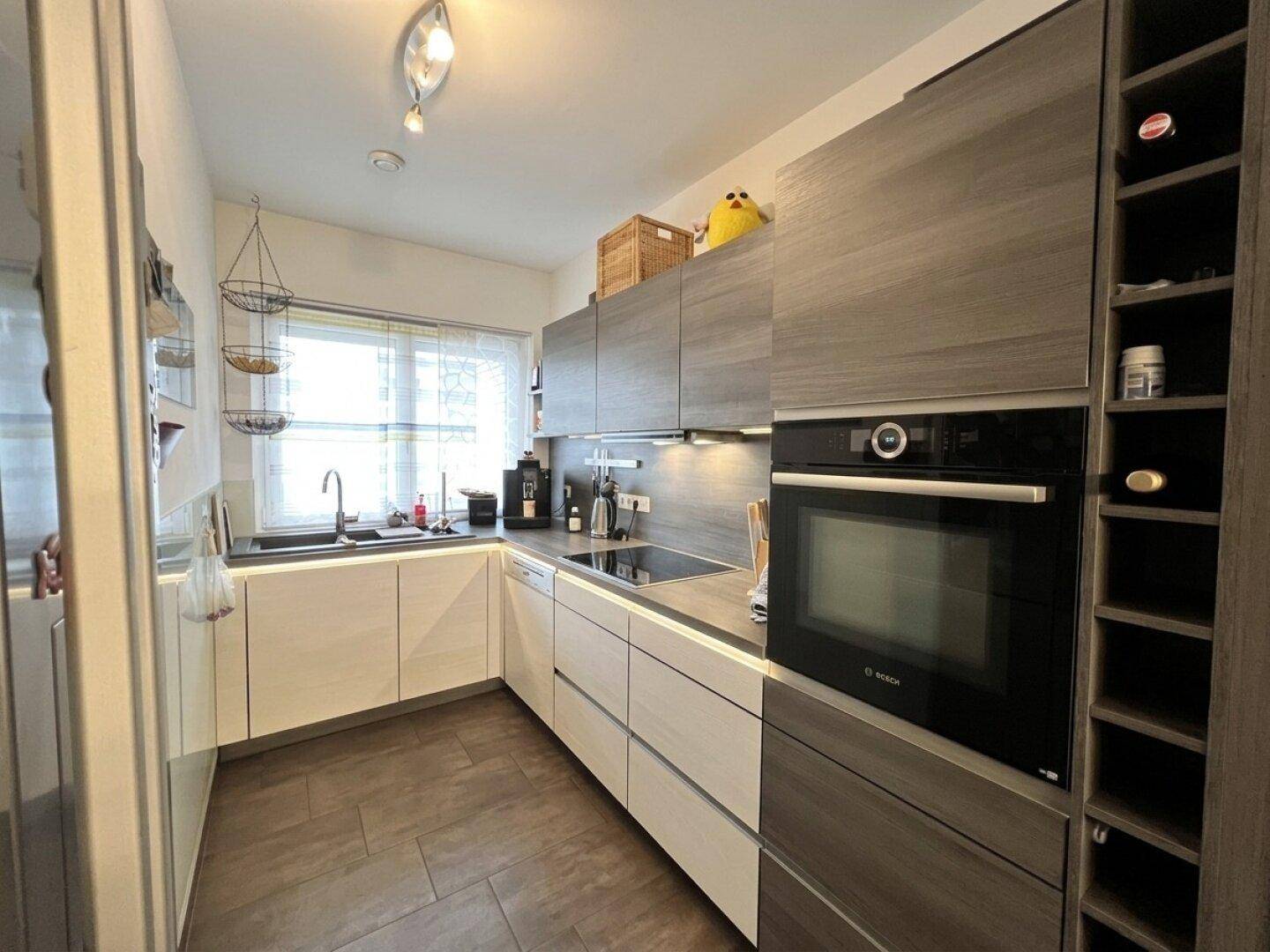 Moderne Küche mit zweifarbigen Schränken, integriertem Backofen und Fenster für natürliches Licht.