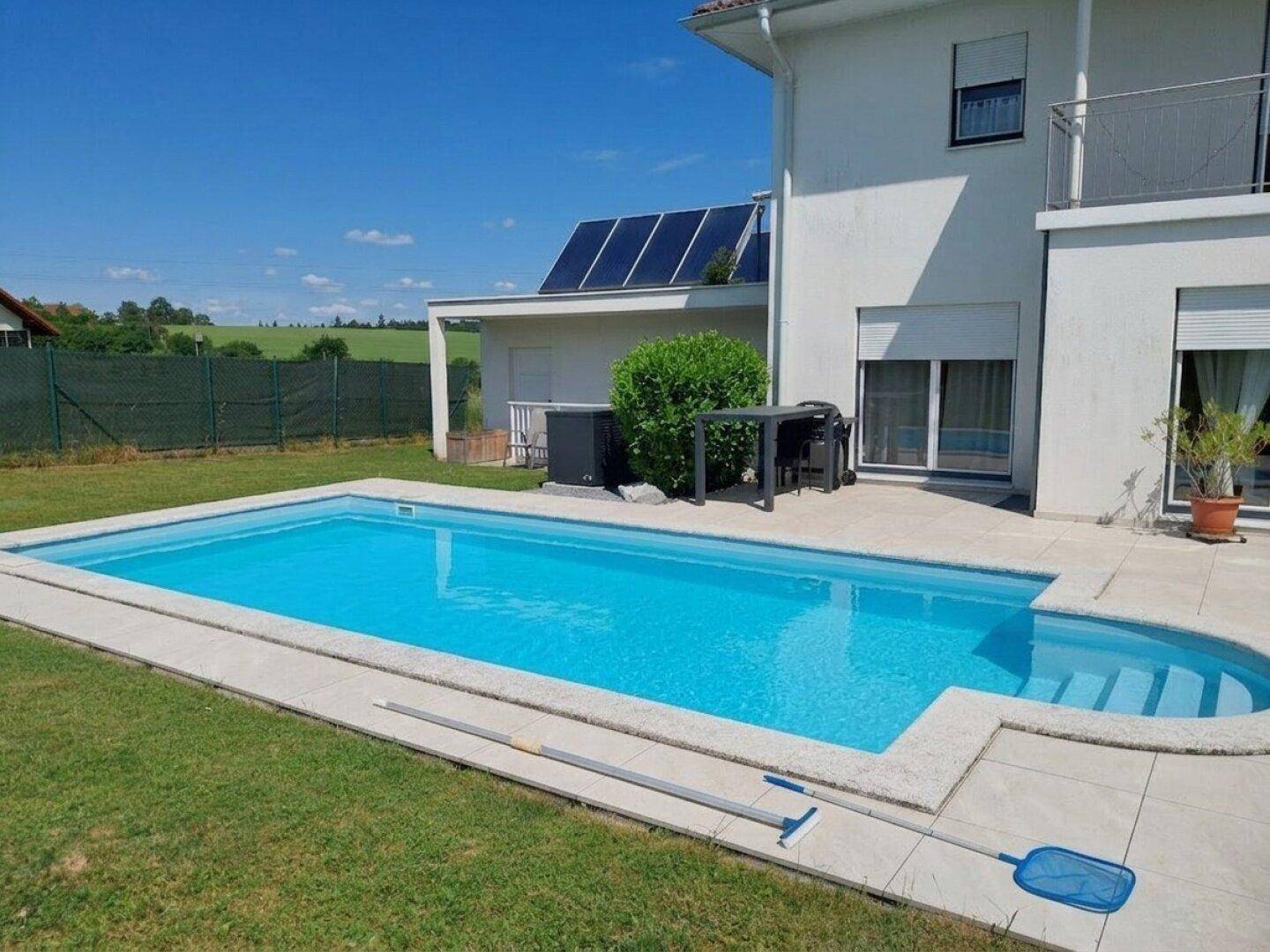 Rechteckiger Pool mit gefliester Terrasse und Rasenfläche im Gartenbereich des Hauses.