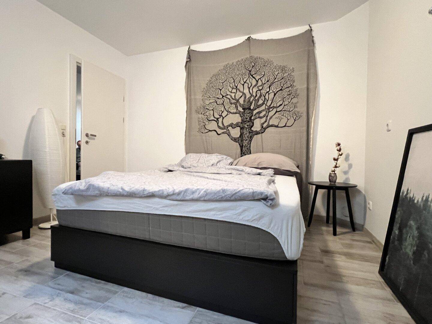 Schlafzimmer im Keller mit Doppelbett und dekorativem Wandteppich, gemütlich eingerichtet.