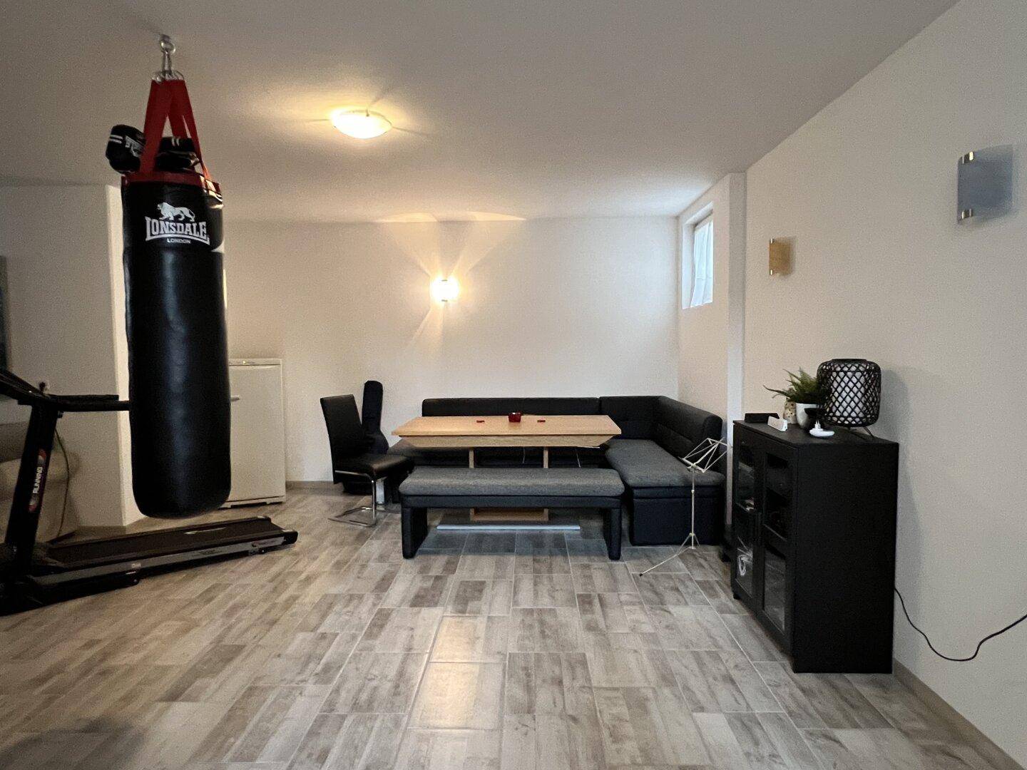 Vielseitiger Kellerraum mit Essbereich, Fitnessgeräten und Boxsack, funktional eingerichtet.