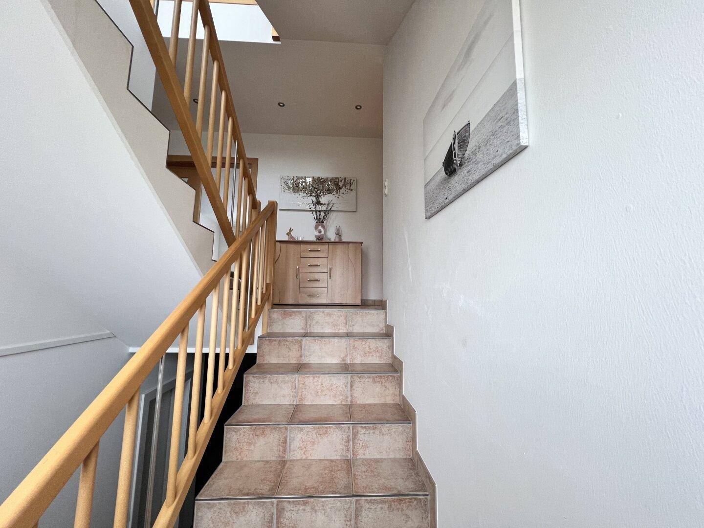 Treppenhaus mit Holzgeländer und gefliesten Stufen, führt in die obere Etage des Hauses.