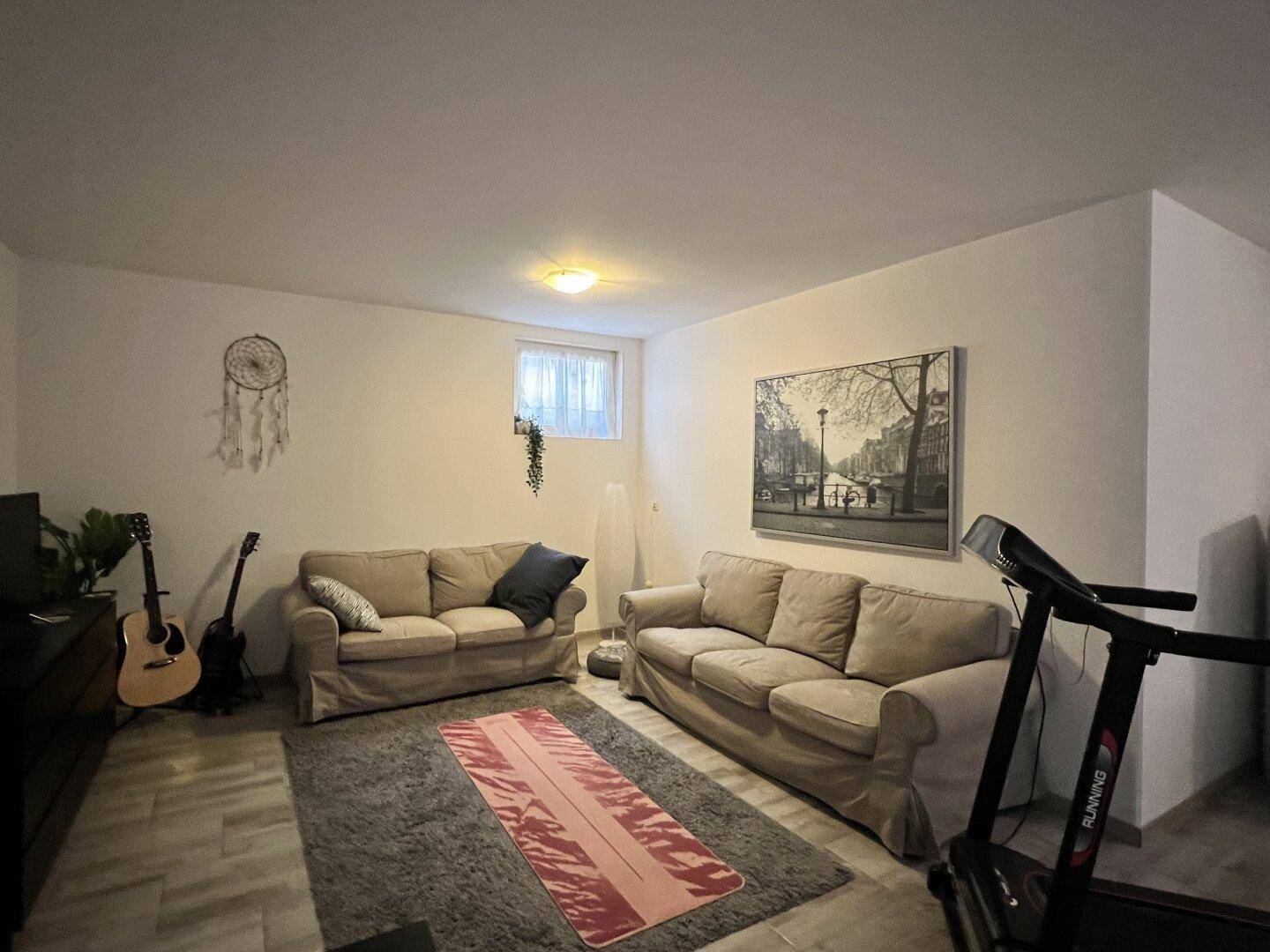 Gemütlicher Wohnbereich im Keller mit Sofas und kleinem Fenster, gut beleuchtet.