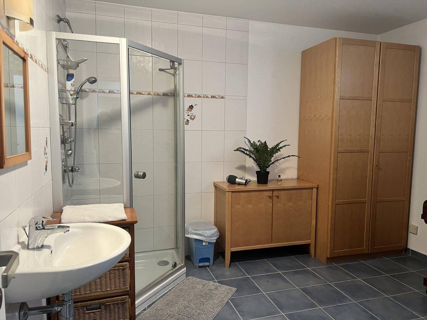 Badezimmer im Keller mit Duschkabine, Waschbecken und Holzschränken, praktisch gestaltet.