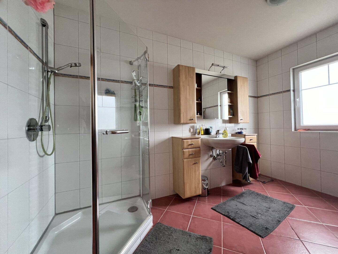 Badezimmer mit Duschkabine, Einzelwaschbecken und hellen Fliesen, ausgestattet mit Fenster.