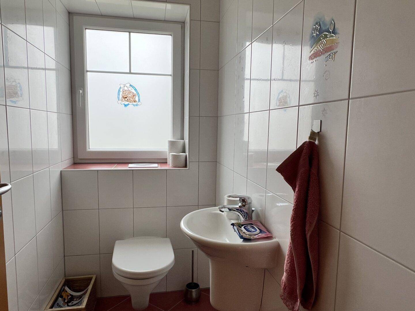 Kleines Gäste-WC mit Fenster, Toilette und Waschbecken, komplett gefliest.