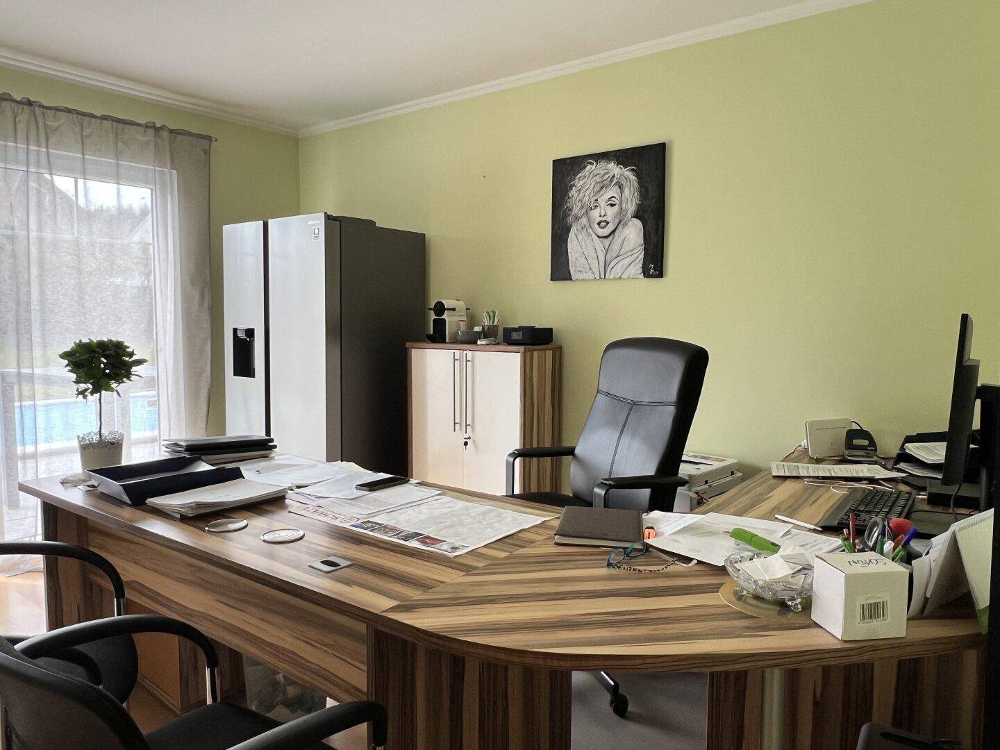 Helles Büro mit großem Schreibtisch, grün gestrichenen Wänden und Blick ins Grüne.
