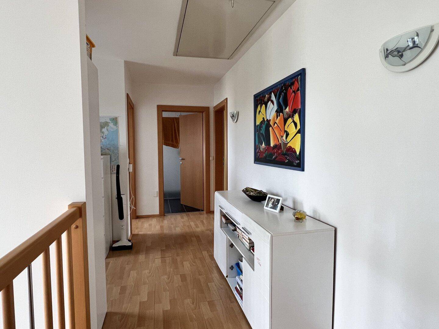 Heller Flur im Obergeschoss mit Holzfußboden und moderner Kommode, gut beleuchtet.