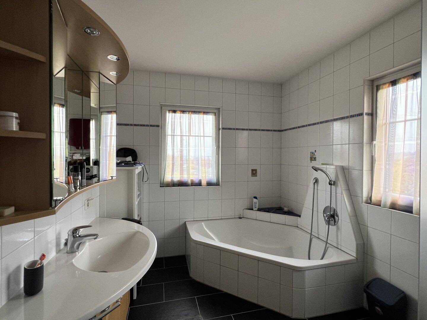 Badezimmer mit Eckbadewanne, Einzelwaschbecken und weißen Fliesen, inklusive Fenster.