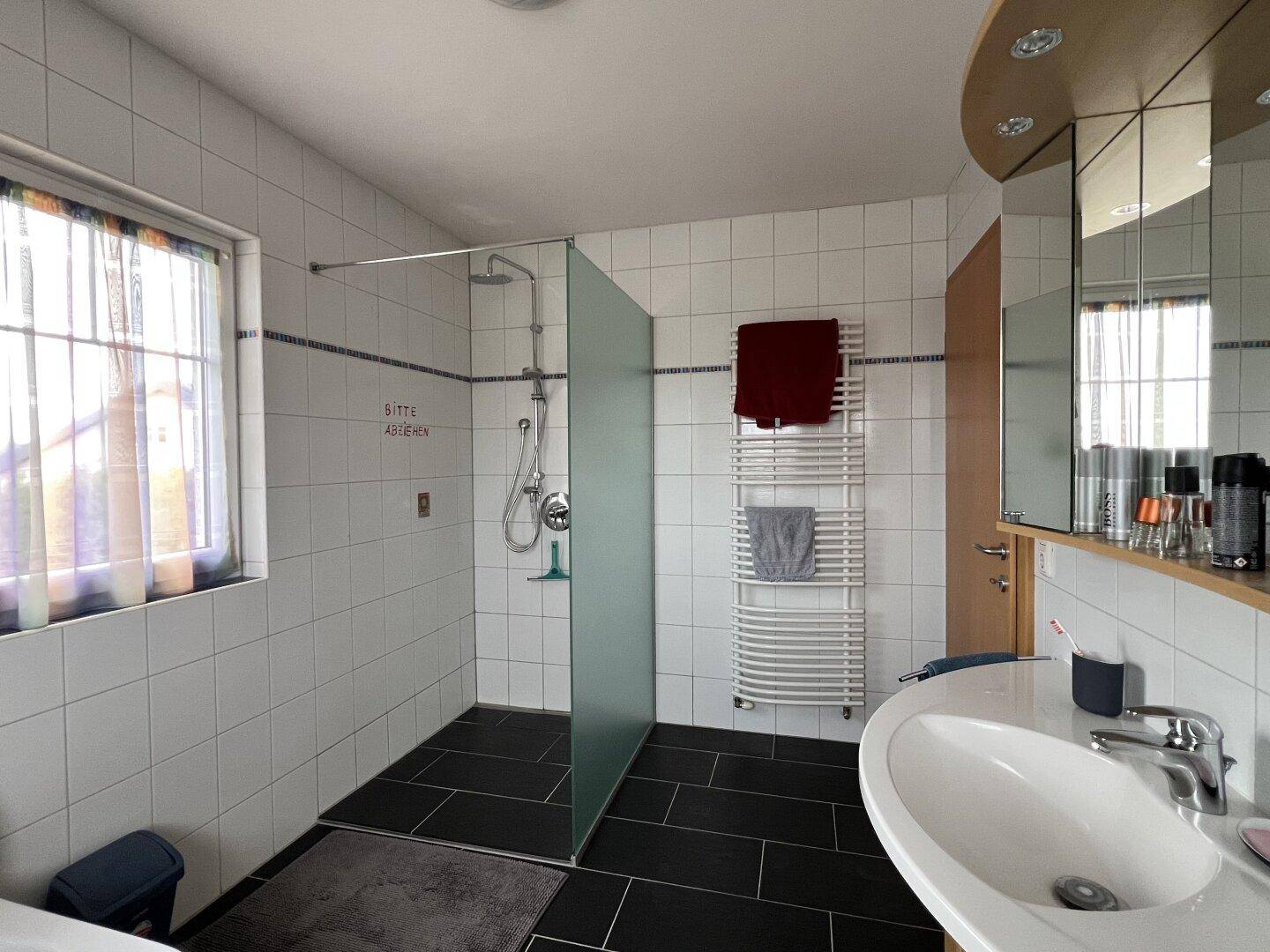 Modernes Badezimmer mit begehbarer Dusche, Handtuchheizkörper und Fenster für Tageslicht.