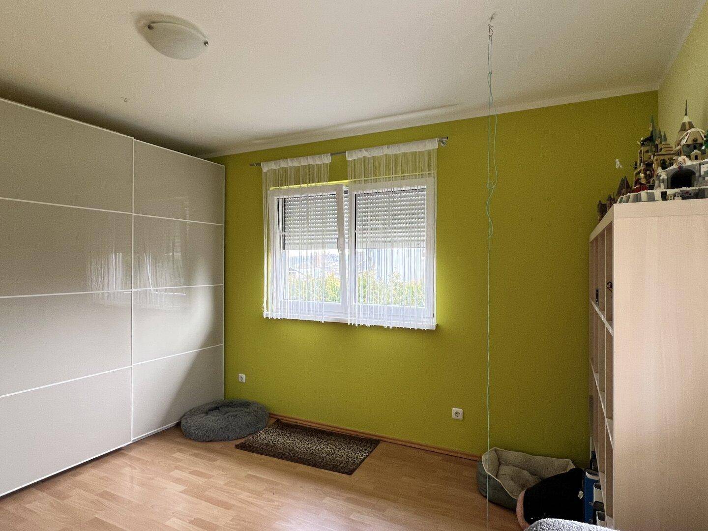 Kinderzimmer mit grün gestrichenen Wänden, Laminatboden und großem Fenster.