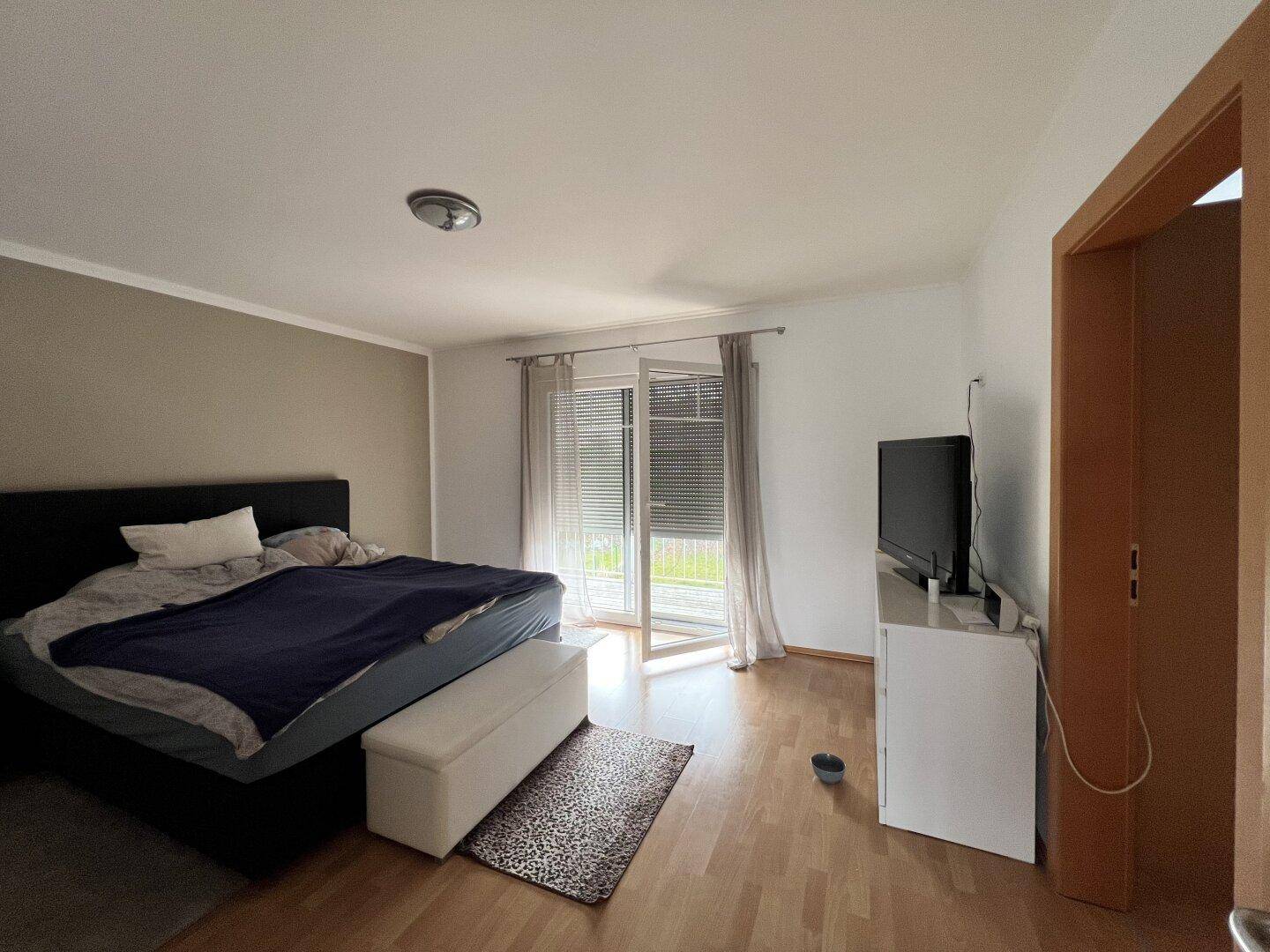 Schlafzimmer mit Doppelbett, Laminatboden und Zugang zum Balkon für frische Luft.