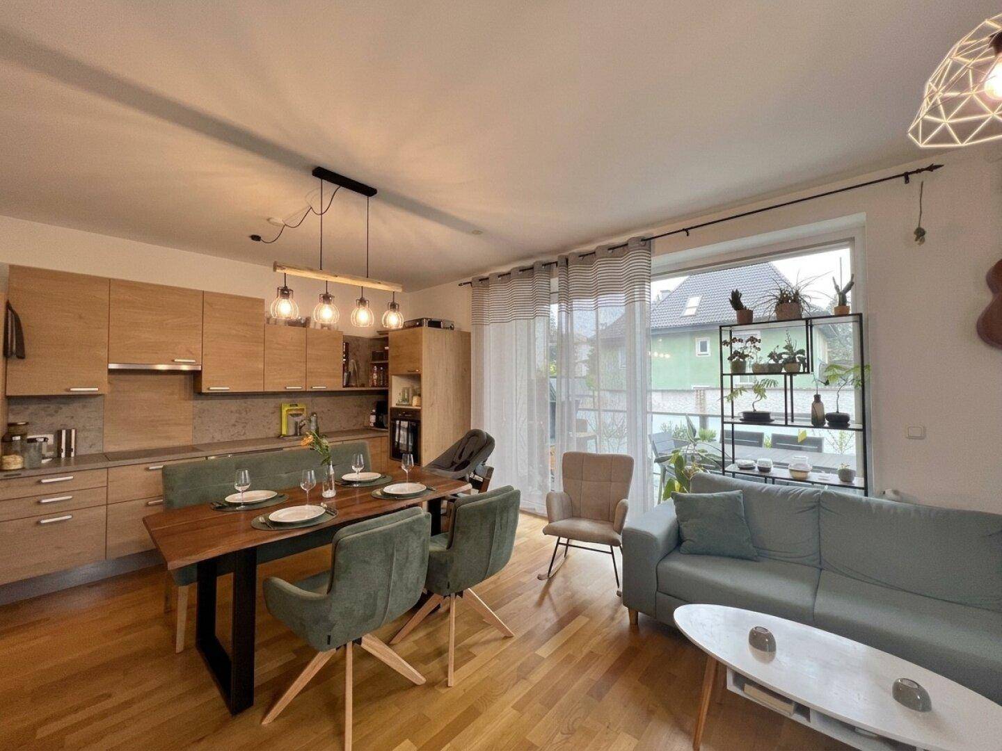 Heller offener Wohn-Essbereich mit moderner Holzküche, Esstisch und gemütlichem Sofa.