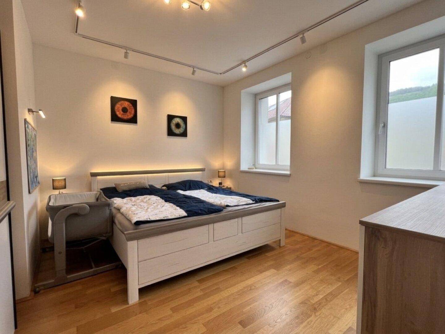 Helles Schlafzimmer mit Doppelbett, Holzboden und zwei Fenstern für eine angenehme Atmosphäre.