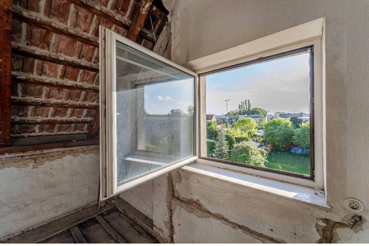 Dachboden im Rohzustand mit offenem Fenster und Blick ins Grüne, bereit zur Renovierung.