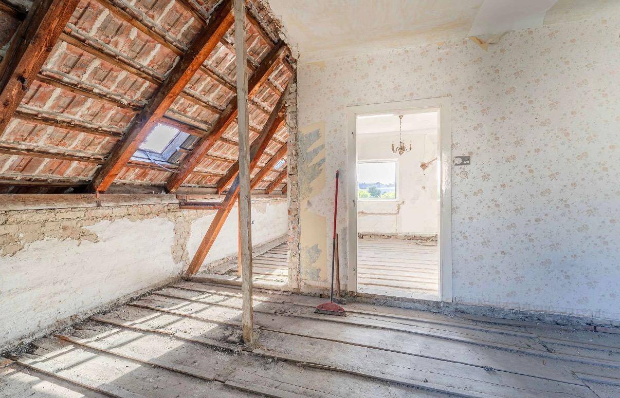 Unausgebauter Dachboden mit sichtbaren Dachbalken, Holzboden und Dachfenster.