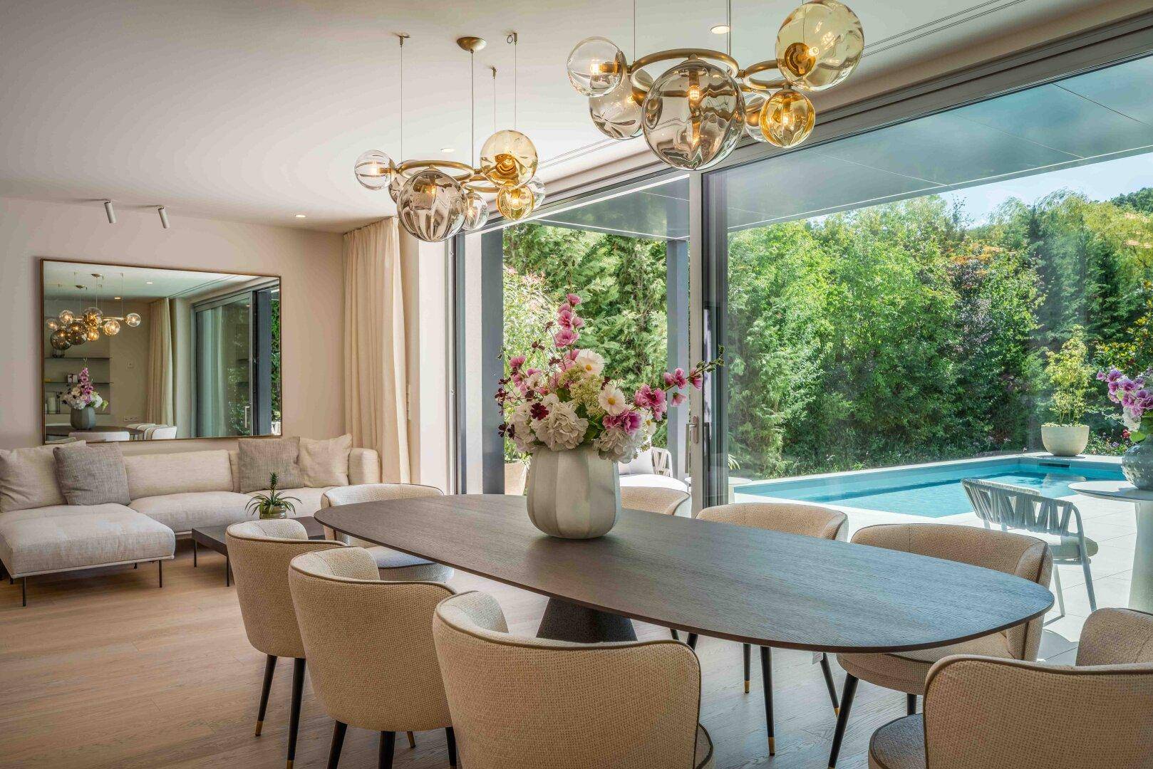 Eleganter Essbereich mit modernem Kronleuchter und großen Glasfronten, die den Blick auf den Pool freigeben.