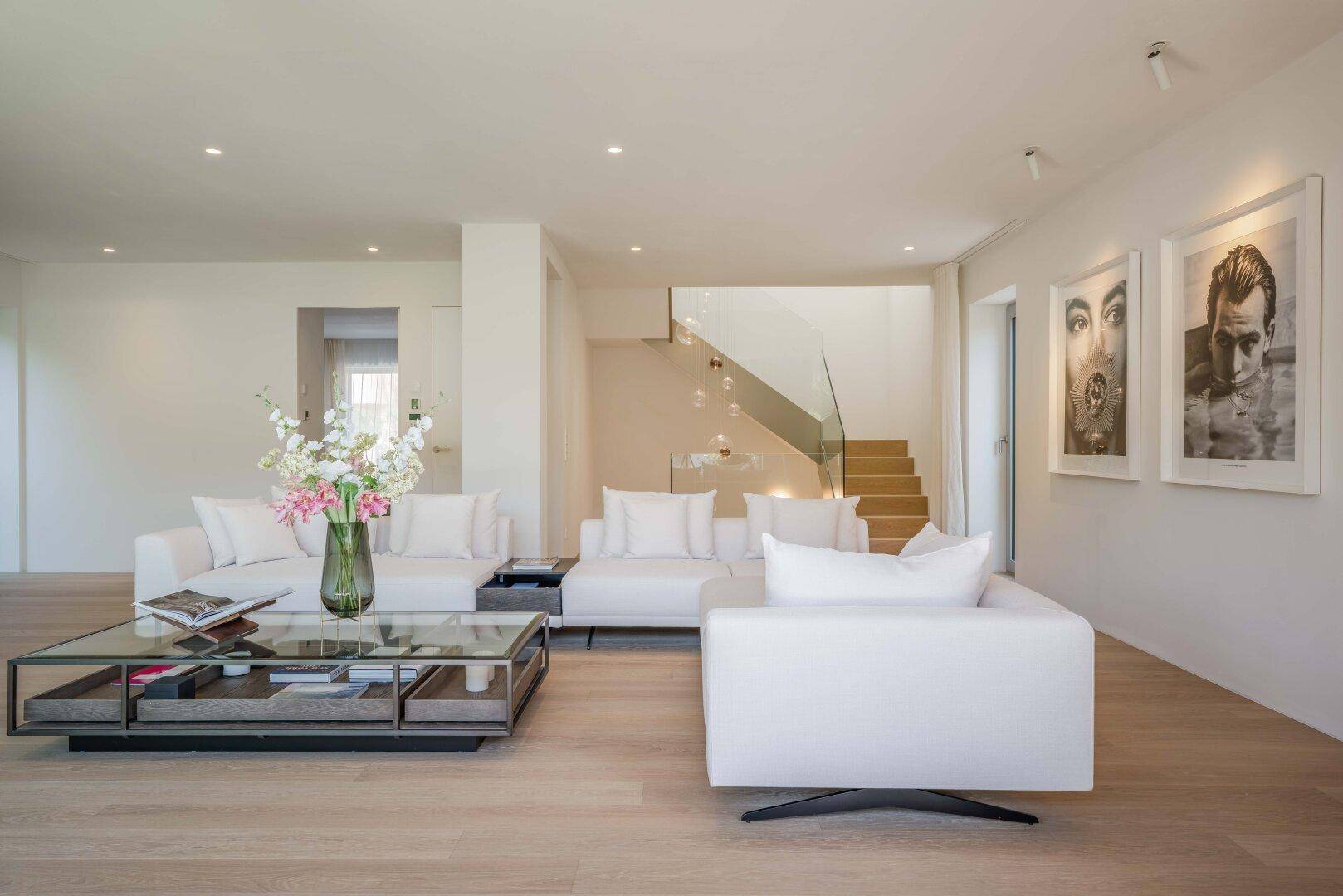 Geräumiges Wohnzimmer mit stilvollen Möbeln und einer modernen Treppe mit Glasgeländer.