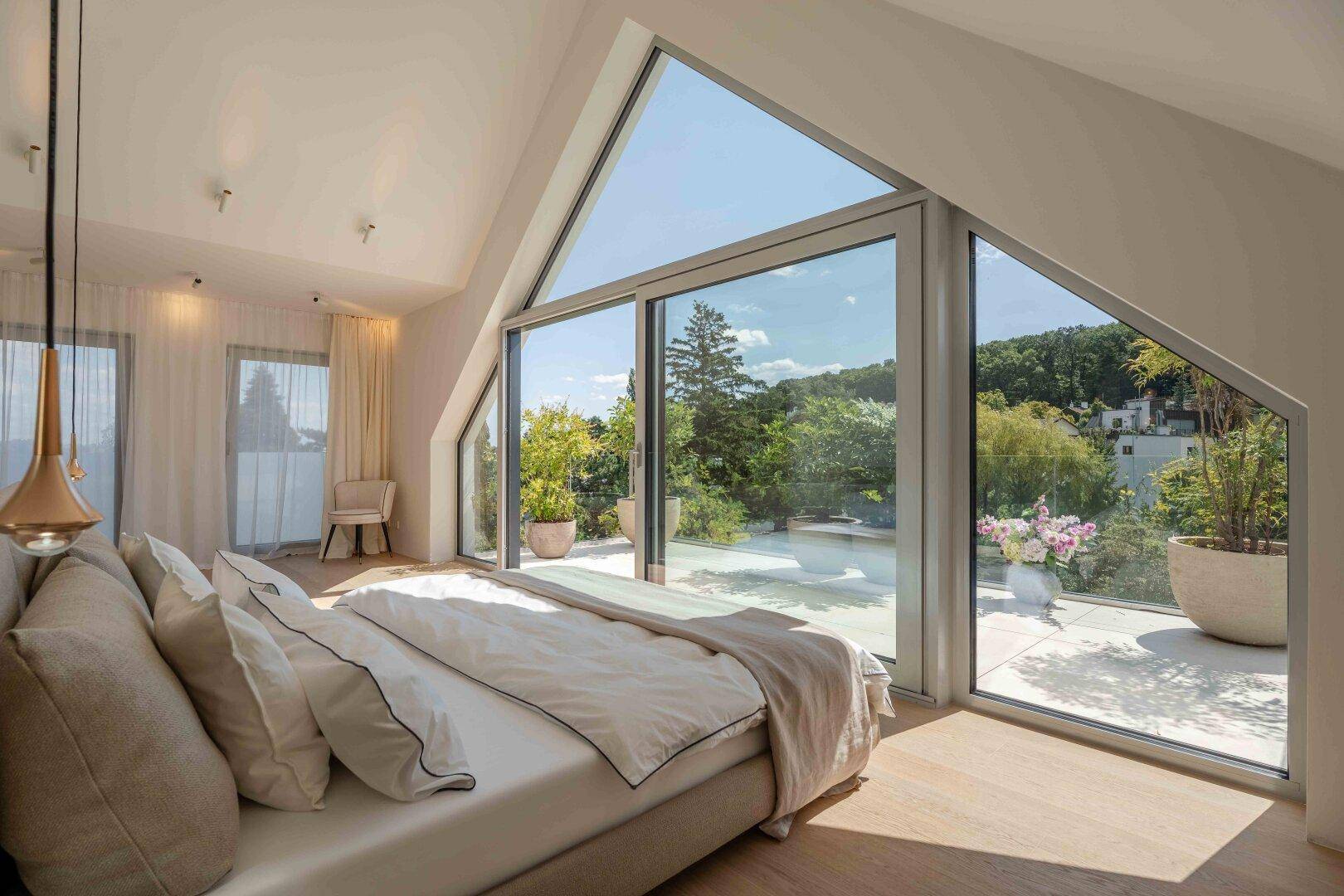 Helles Schlafzimmer im Dachgeschoss mit großen Fenstern, Dachschräge und Zugang zur Terrasse.