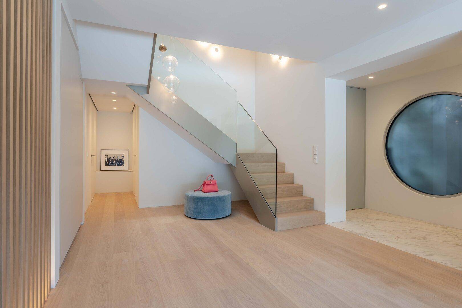 Heller Flur mit moderner Glas-Treppe, Holzboden und stilvoller Dekoration.