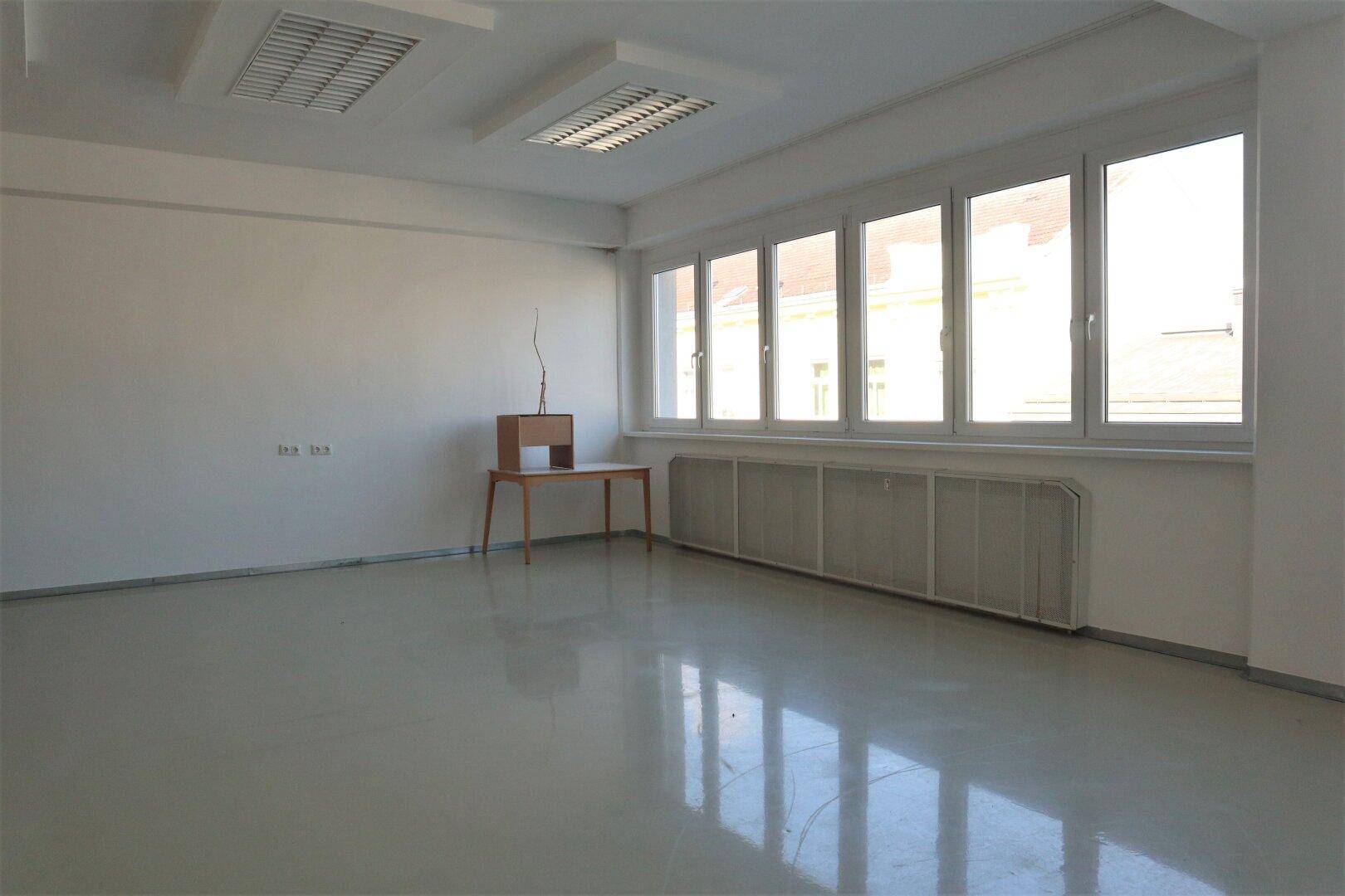 Leerer, heller Raum mit großen Fenstern und einem kleinen Tisch, ideal für ein ruhiges Büro oder Arbeitszimmer.